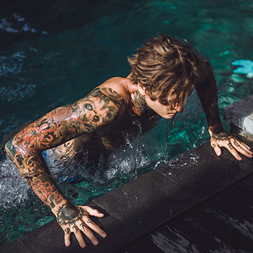 young handsome man in tattoos resting in the outdoor pool. A tattooed man in the pool is having fun. on bali, indonesia